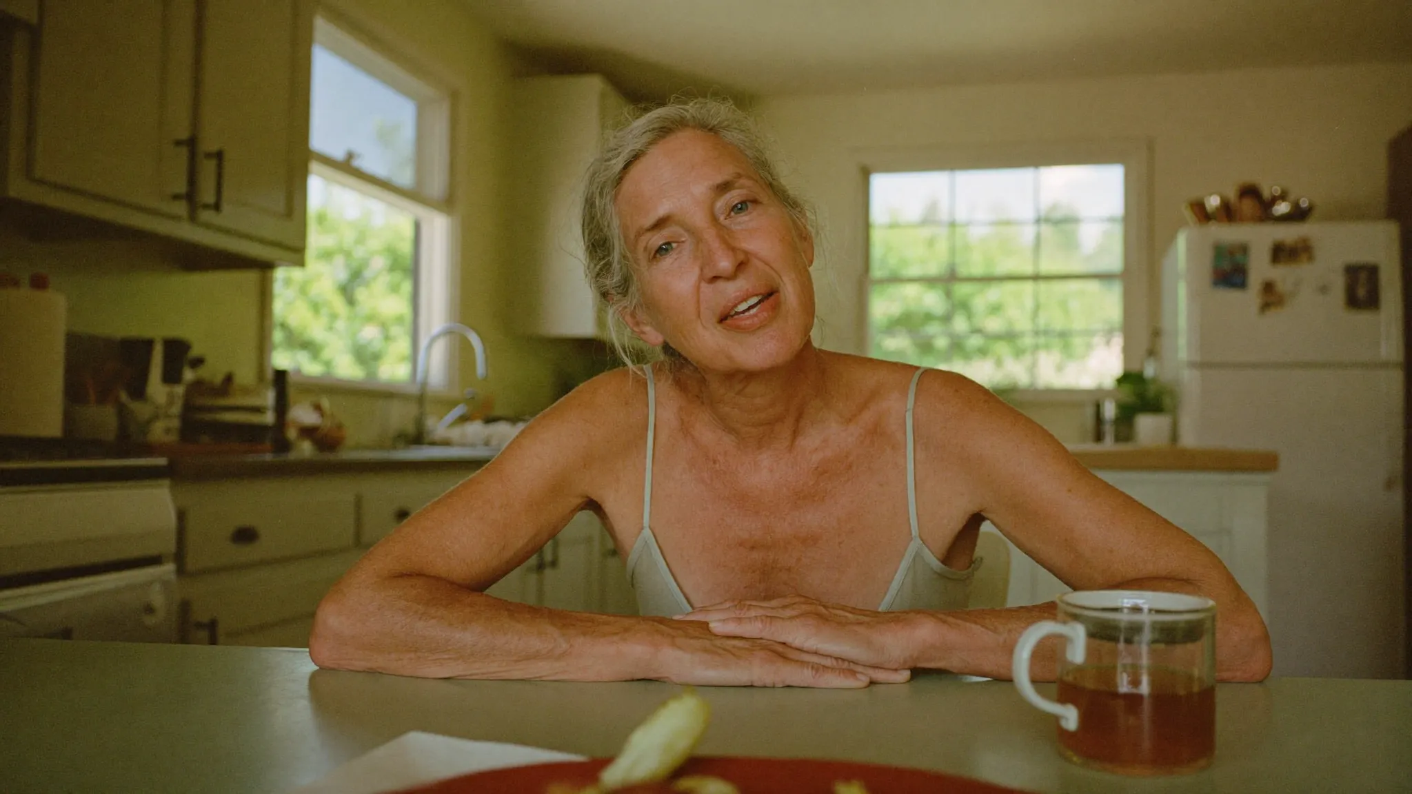 A woman in her mid 40s at her own kitchen table, speaking straight to camera in morning light